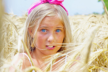 Summer holiday concept. Beautiful young blonde girl with blue eyes against golden wheat field.