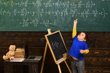 Tiptoeing boy pointing up with chalk in classroom. Small kid learning math. Early development concept