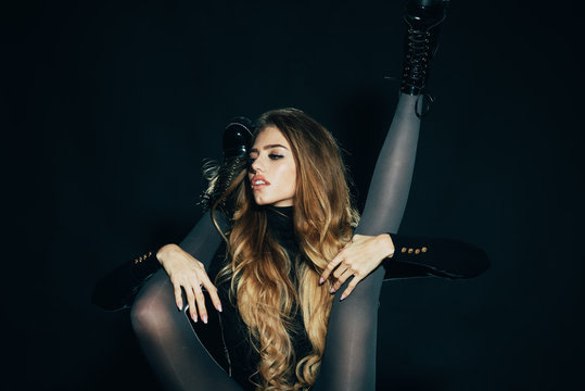Fashionable lady with make up and skinny legs in shoes. Girl with long hair holds legs of another woman, black background. Legs slender in tights and black brutal boots. Shoes advertising concept.