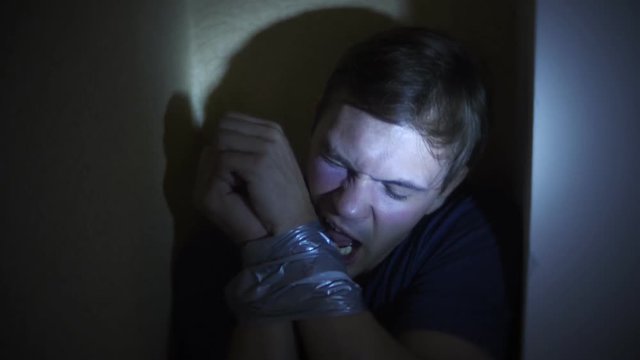 violence, crime, kidnapping and people concept - criminal tying man hands with adhesive tape. 4k, semi-dark