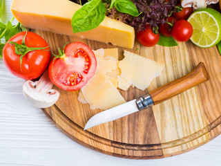 Appetizing still life. Fresh cherry tomatoes, lettuce leaves, mushrooms, green basil, cheese on wooden board. The knife for cutting vegetables.