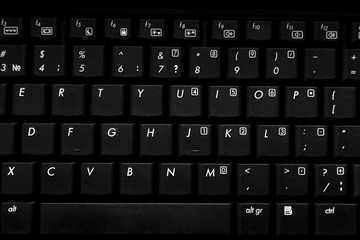 Black laptop keyboard with white letters and touchpad view from above with shallow depth of field.
