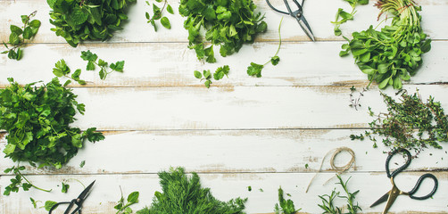 Flat-lay of bunches of various fresh green herbs. Parsley, mint, dill, cilantro, rosemary, thyme over wooden background, top view, copy space, wide composition. Healthy vegan cooking concept