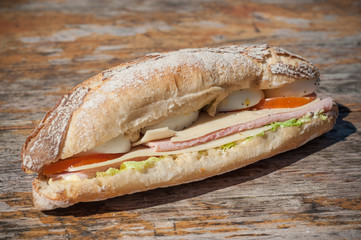 closeup of french sandwich with ham, cheese and vegetables on wooden table background