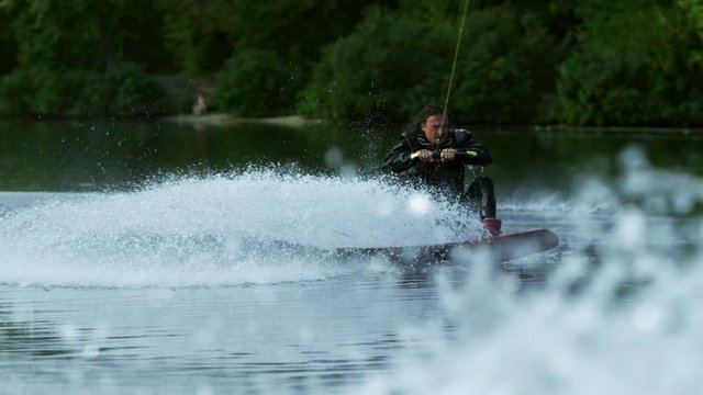 Wakeboarder making tricks on waves during movement in slow motion. Joyful man riding wakeboard in water splash. Athlete water skiing and have fun. Extreme water sports