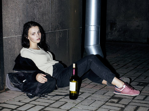 young poor ttenage girl sitting at dirty wall on floor with bott