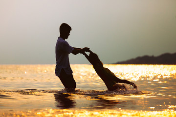 Silhouette of asian father carrying his daughter turn around and playing together in the sea with sunset in summer vacation