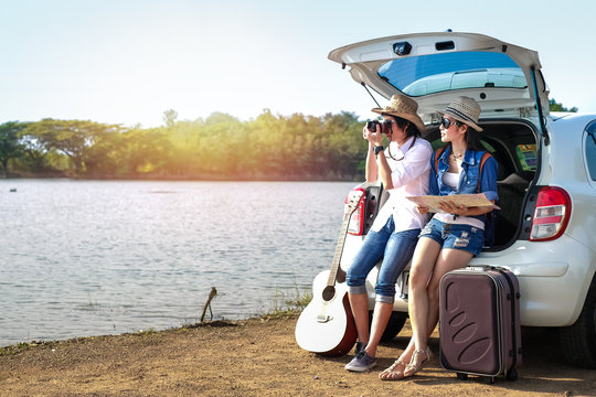 Couple of traveler sitting on hatchback of car and enjoying for view of nature near the lake during holiday.Young couple tourist have a guitar and baggage taking photo on vacation. 