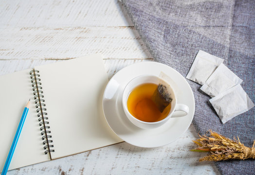 A cup of hot herbal tea with note book on white wooden table.