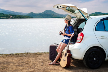 woman traveler sitting on hatchback of car and looking to local map near the lake during holiday background is the mountain.Young lady tourist enjoying for view of nature on vacation. 