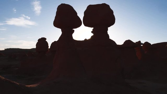 Upward tilt viewing hoodoos in Goblin Valley as the sun peaks over the edge at sunset.