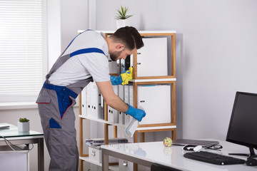 Man Cleaning Desk In Office