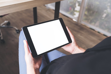 Top view mockup image of a woman sitting cross legged and holding black tablet pc with blank white desktop screen