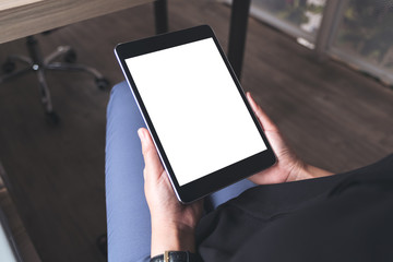 Top view mockup image of a woman sitting cross legged and holding black tablet pc with blank white desktop screen
