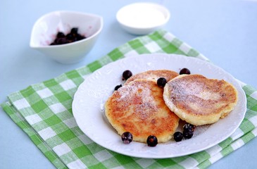 Breakfast. Curd cheese cakes with sour cream and currants sprinkled with powdered sugar.