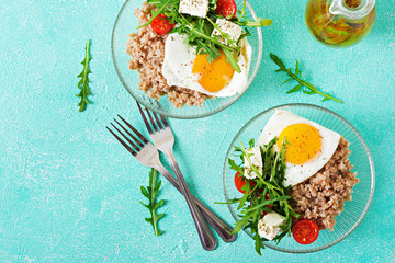 Healthy breakfast with egg, feta cheese, arugula, tomatoes  and buckwheat porridge on light background. Proper nutrition. Dietary menu. Flat lay. Top view
