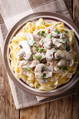 Noodles with creamy sauce, mushrooms, bacon and onions close-up on a plate. Vertical top view