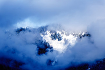 Sun shining through the clouds on the Snow Capped Peak of Coquitlam Mountain in the Coast Mountain Range seen from the shore of Pitt Lake in the Fraser Valley of British Columbia, Canada