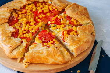 Tomato and sweet corn galette on a wooden board. Close up. White stone background.