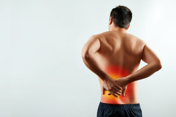 The man holds his hands behind his back, pain in the kidneys, pain in his back. Light background. The concept of medicine.