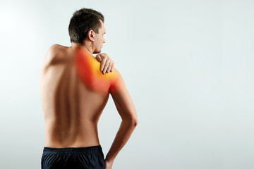 A man holds his hands for a damaged shoulder, a pain in his shoulder highlighted in red. Light background. The concept of medicine.