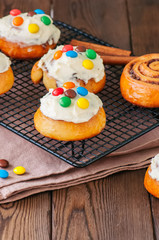Classic cinnamon rolls - cinnabons with cream cheese frosting with smarties. Wooden background.