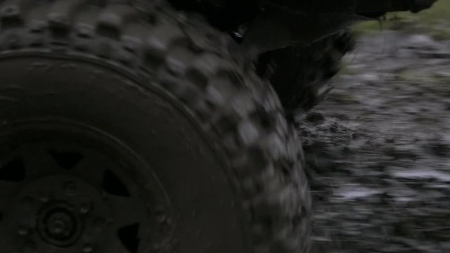 Close up, slow motion shot of off-road vehicles front entering very muddy terrain, splashing mud around and driving away.