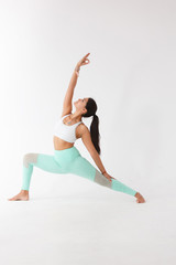 Beautiful graceful young woman in gymnastic costume doing pilates, yoga exercise or gymnastics for stretching hands and feet on white isolated background