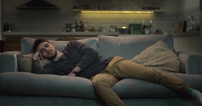 Relaxed man lying comfortably on a sofa watching tv.