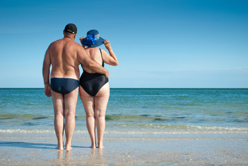 elderly couple standing on the seashore holding hands romance bathing suits cap melt straw hat beach beach sand rest summer weekend