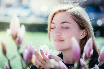 Obraz premium Junge hübsche Frau schnuppert an Magnolien-Blüte, Frühling