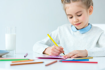 portrait of kid drawing greeting postcard for mother with colorful pencils at table, mothers day holiday concept