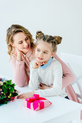 mother hugging daughter at table with gift box and bouquet, happy mothers day concept