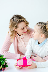 portrait of smiling mother hugging little cute daughter with wrapped gift in hands, mothers day holiday concept