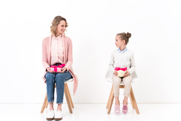 Fototapeta premium mother and daughter sitting on chairs and holding present boxes, happy mothers day concept