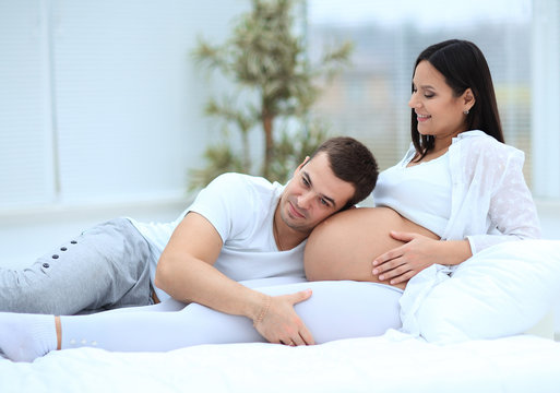 Husband listening to his wife's belly at home
