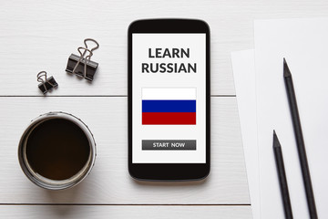 Learn Russian concept on smart phone screen with office objects on white wooden table. All screen...