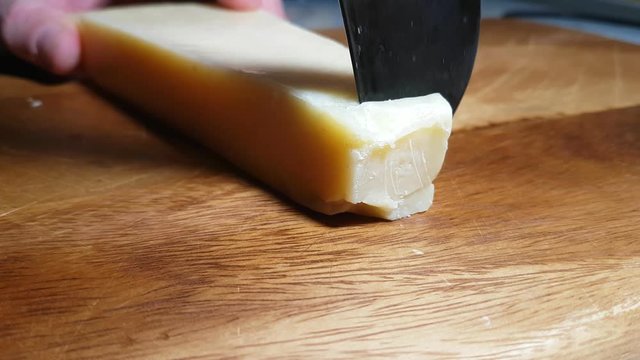 knife cuts parmesan cheese on wooden