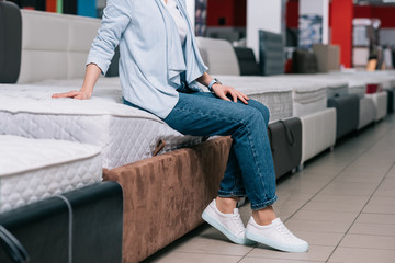partial view of woman sitting on mattress in furniture shop - obrazy, fototapety, plakaty