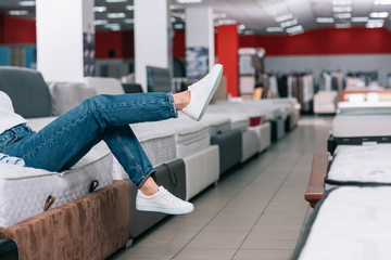 partial view of woman sitting on mattress in furniture shop