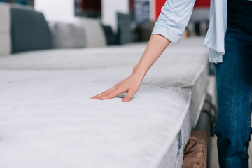 partial view of woman touching orthopedic mattress in furniture shop