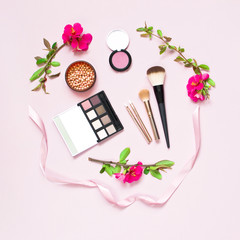 Various cosmetic products eye shadow powder lip gloss blush mascara brush for makeup and pink spring flowers on a pink pastel background top view with copy space