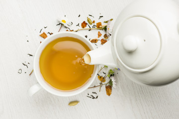 Gießen von Tee mit Teekanne in Tasse auf weißem Tisch