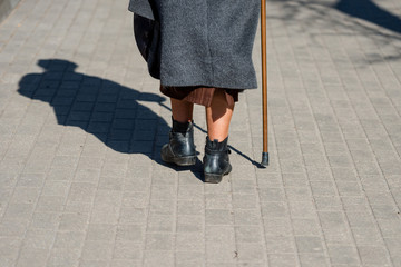 On a sunny day a old woman walking down the street with walking stick. The woman's shadow is...