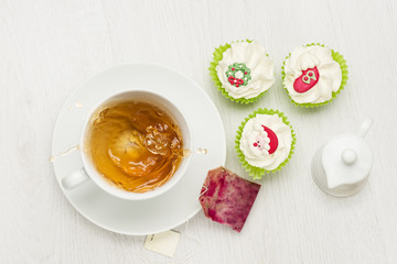 cup of splashing tea on white table with tea bag and christmas cupcakes