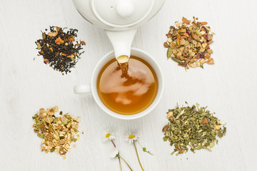 pouring tisane into cup with variety of herbal tea on table