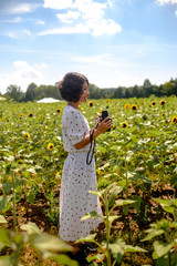 Girl  in the sunflowers field holding old vintage camera taking photo enoying the sun picking up flower dancing laughing spinning and talking with big smile / red lip stick