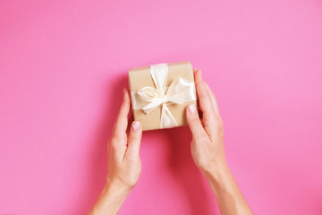 Close up of female hands holding birthday gift in vintage craft paper wrapping. Femenine composition with present in woman's arms.