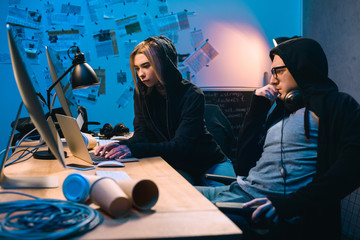 couple of young hackers using laptop at workplace in dark room