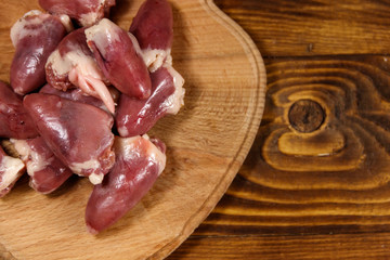 Raw chicken hearts on cutting board on wooden table